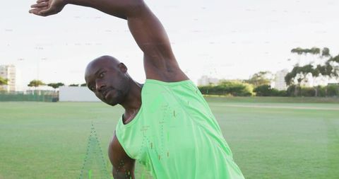 African american man stretching side bend in neon green tank top on outdoor sports field