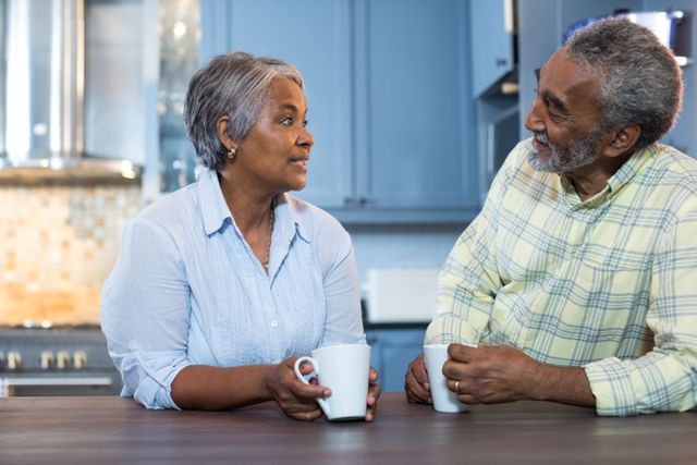 Senior couple enjoying coffee and conversation in kitchen at home. Ideal for use in advertisements, articles, and blogs related to senior living, healthy relationships, home life, and morning routines.