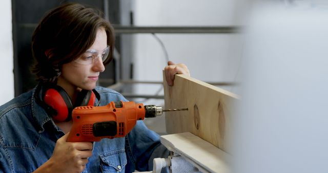 Young Caucasian woman drills a shelf at home, with copy space. She wears safety glasses while focusing on her DIY project.