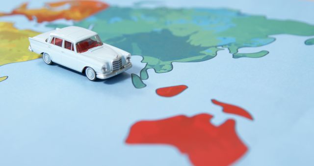 White toy car positioned on partially visible colorful world map indicating various continents. Ideal for use in travel blogs, educational materials, global adventure concepts, transportation themes, international business, wanderlust inspiration.