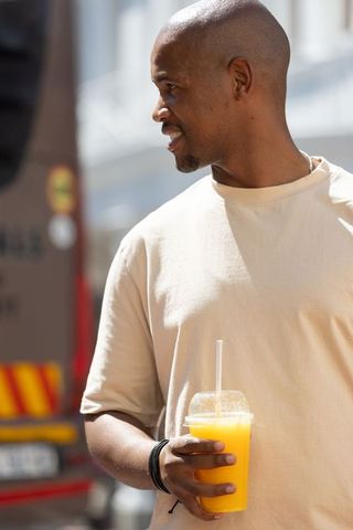 African american man holding orange juice cup and looking right on sunlit urban street