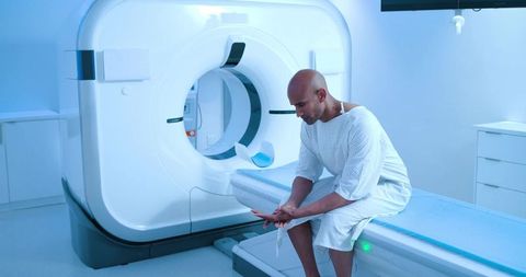 African american man sitting on ct scanner table awaiting scan in sterile radiology suite