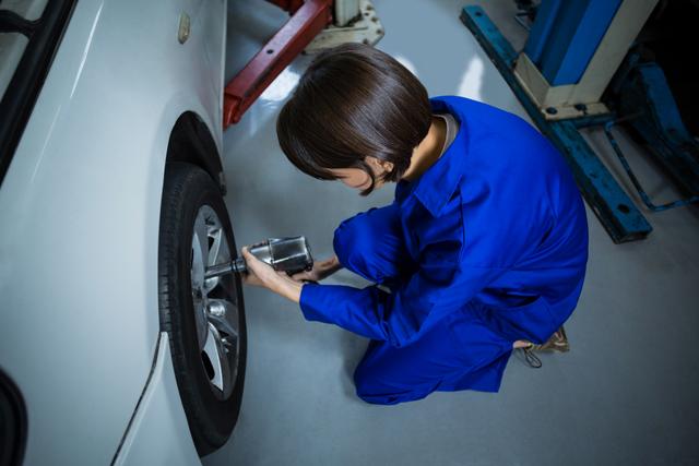 Female mechanic fixing a car wheel with pneumatic wrench in repair garage