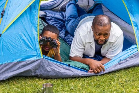 African american father and son camping in blue tent observing nature with binoculars