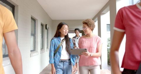 Teenagers discussing with tablet while walking in school