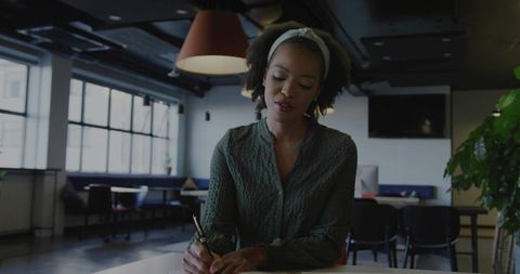 African american woman writing at modern coworking desk, focused professional work