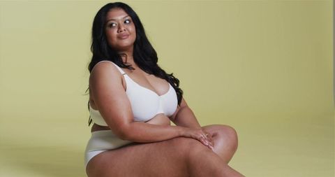 Confident Asian Woman in Elegant Neutral Underwear Poses on Yellow Background