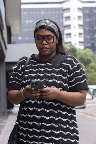 African woman using smartphone while walking urban street wearing sunglasses and headband
