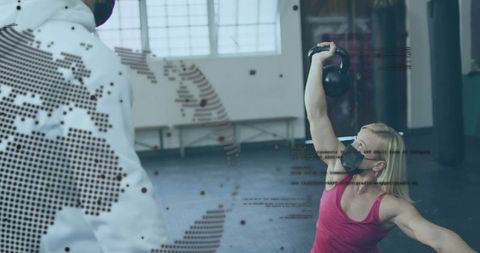 Masked woman performing single-arm kettlebell press in gym with digital world map overlay