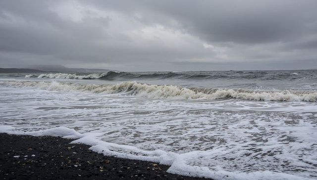 Crashing ocean waves rolling toward pebble shoreline under dramatic overcast sky