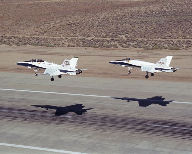 Two NASA F/A-18 fighter jets landing on runway at Edwards Air Force Base after Autonomous Formation Flight mission. Useful for content related to aviation technology, aerospace research, military aircraft, autonomous systems, and NASA missions.