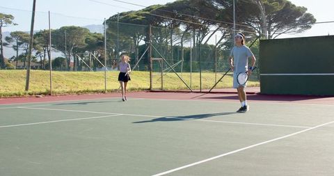Asian players practicing tennis on outdoor hard court with backboard and rackets