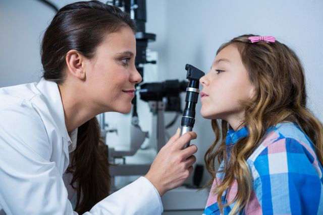 Female optometrist examining young patient with ophthalmoscope in ophthalmology clinic. Useful for illustrating healthcare services, pediatric eye care, medical examinations, and professional healthcare environments.