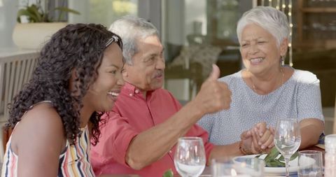 Senior couple and African American woman enjoying outdoor dinner, man giving thumbs-up