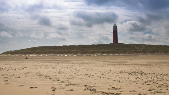 Dramatic lighthouse standing tall on a sandy beach under a cloudy sky. Ideal for showcasing coastal beauty, serenity, and isolated landscapes. Great for travel blogs, tourism promotions, and nature-themed projects.