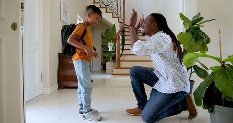 Father Tying Son's Shoe Laces Before School in Home Hallway