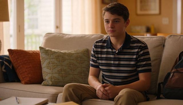 Teen boy sitting on cozy living room sofa studying with backpack and notebook