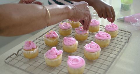 African american grandmother and granddaughter decorating pink frosted cupcakes together