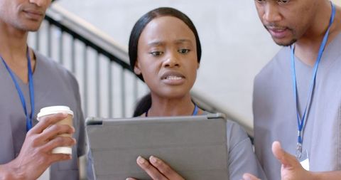 African american nurses collaborating on tablet reviewing clinical notes holding coffee