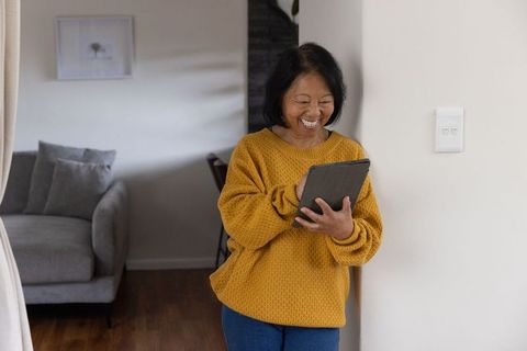 Smiling senior asian woman using tablet in modern home environment
