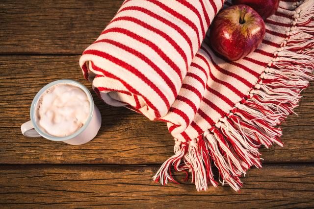 Rolled blanket with two apples and coffee mug on wooden table