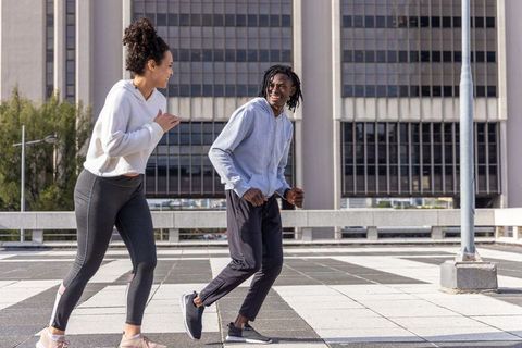 Jogging and laughing friends on rooftop plaza wearing hoodies, leggings, joggers, sneakers