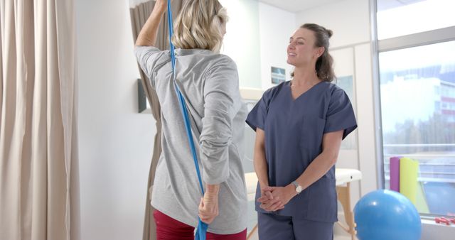 Senior woman performing physical therapy exercises under the guidance of a therapist in a well-lit clinic. The elderly patient engages in a stretching routine with support, showcasing themes of health, recovery, and professional care. This image is ideal for use in healthcare articles, rehabilitation brochures, wellness programs, and promotional materials for physical therapy services.