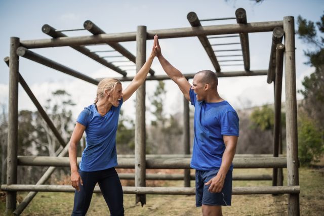 Fit woman and man giving a high five to each other during obstacle course in boot camp