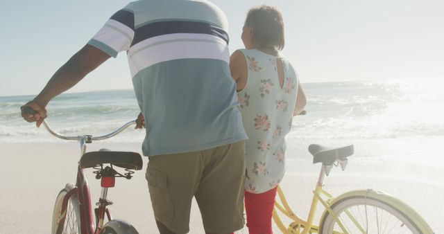 Senior african american couple walking with bicycles on sunny beach - Download Free Stock Photos Pikwizard.com