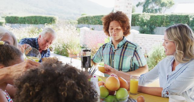 Family members having breakfast together outdoors, enjoying fresh fruits and orange juice. Perfect for themes related to family bonding, outdoor activities, summer gatherings, healthy living, and casual meals.