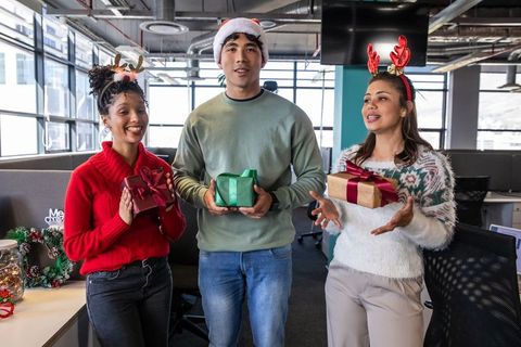 Diverse coworkers exchanging holiday gifts and wearing reindeer antlers in office