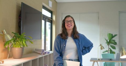 Young professional smiling in modern coworking space holding laptop, casual denim shirt