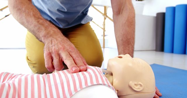 A middle-aged Caucasian man is practicing CPR on a training dummy, with copy space. His focus on the dummy indicates a first aid training session or a demonstration of life-saving techniques.