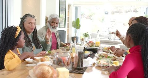 Multigenerational family sharing sunlit brunch around wooden table with bread and butter