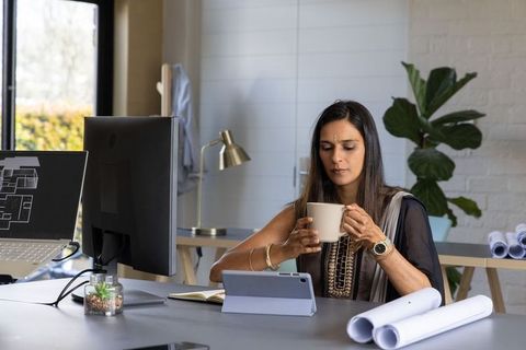 Indian architect reviewing tablet holding coffee in modern studio with blueprints