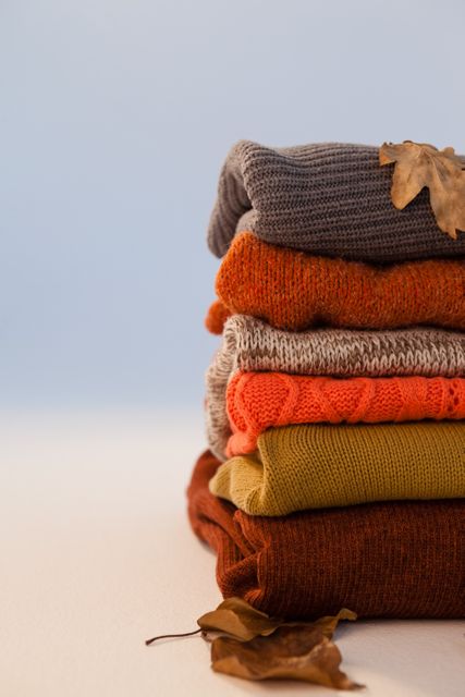 Stack of woolen clothing with autumn leaves on white background