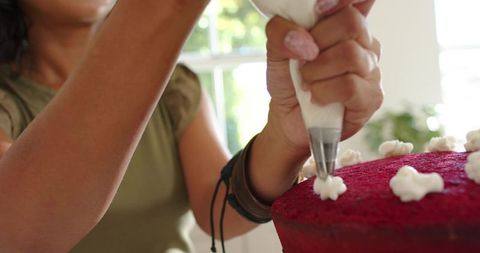 Home baker decorating red velvet cake, piping frosting stars at sunlit window