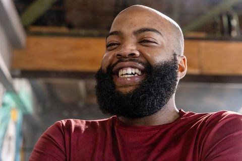 Joyful african american man laughing in industrial workshop wearing maroon t-shirt closeup