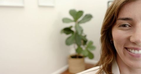 Smiling professional woman wearing blazer in minimal home office with fiddle leaf fig