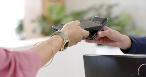 African american customer tapping smartphone for contactless payment at reception counter