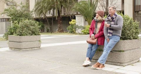 Relaxed mature couple leaning on urban planter enjoying coffee together on overcast day