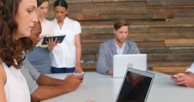 Diverse group of professionals working together on laptops and tablets around table in modern office setting. Ideal for depicting teamwork, collaboration, corporate strategy sessions, and technological integration in business environments.