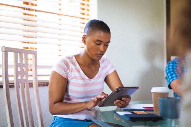 Confident young biracial businesswoman using tablet pc at table inside home. unaltered, people and business concept.
