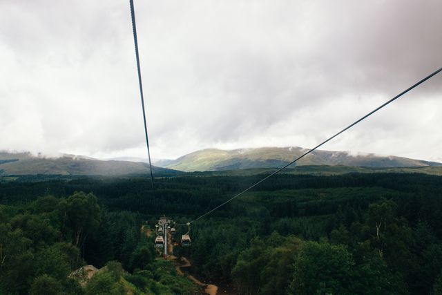 This image depicts a cable car system running through lush green hills and forests under a cloudy sky in the highlands. Ideal for use in travel articles, adventure tourism promotions, landscape photography collections, and brochures showcasing natural beauty and outdoor activities.