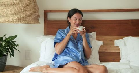 Woman in Satin Pajamas Relaxing with Coffee on Bed