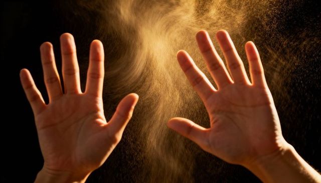 Clapping hands releasing golden dust cloud backlit halo of floating particles