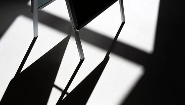 Minimalist metal easel casting geometric shadows on smooth floor high-contrast monochrome