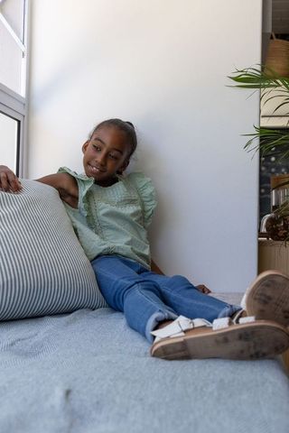 African american teen girl reclining on daybed by window wearing green blouse and sandals