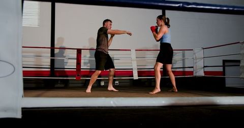 Coach training female boxer sparring in ring throwing jab holding guard barefoot with red gloves