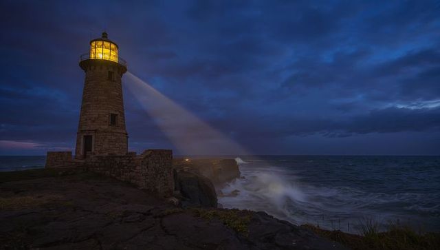 Lighthouse beacon cutting through stormy twilight over rugged rocky coastline